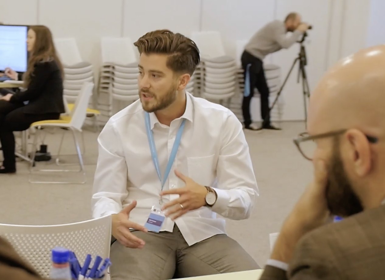 Zoli speaking to a small group seated around a table during a workshop